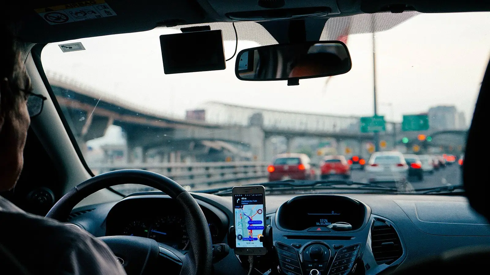 Förare kör bil i morgontrafik med navigering i mobilen på instrumentbrädan